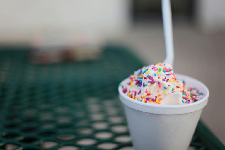 Indulgent vanilla ice cream with colorful sprinkles in a cup on an outdoor table.